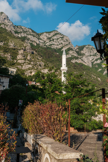 View of a white mosque minaret standing against the rugged Skanderbeg Mountains and lush green trees under a blue sky in Kruje Durres County Albania.