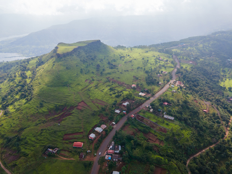 Aerial view of Kaas plateau in the Western Ghats featuring lush green hills a winding road small houses and dramatic cloud shadows in Satara Maharashtra India.