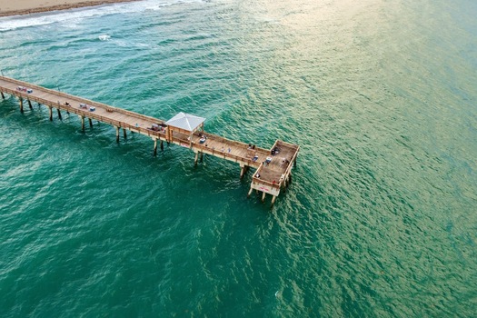 Aerial view of Deerfield Beach International Fishing Pier with people fishing over turquoise ocean water in Deerfield Beach Florida United States.
