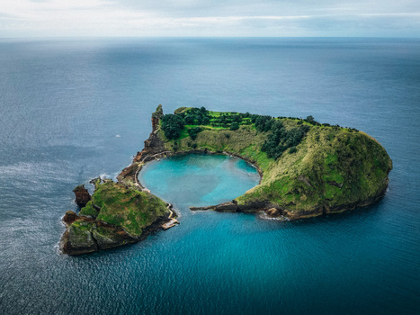 Aerial view of a volcanic crater island with lush green vegetation and turquoise blue lagoon surrounded by the vast deep blue Atlantic Ocean Vila Franca do Campo Portugal.