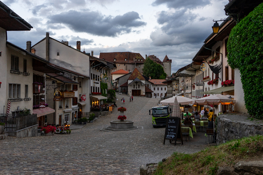 Gruyeres Switzerland 14 May 2026 View of the cobblestone main street lined with historic buildings outdoor cafes and the medieval castle under a cloudy sky. Gruyeres Switzerland 14 May 2026 View of the cobblestone main street lined with historic buildings outdoor cafes and the medieval castle under a cloudy sky.