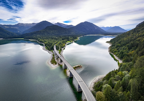 Aerial view of the bridge stretching across the tranquil waters of Sylvensteinsee embraced by verdant forests and majestic mountains Sylvensteinspeicher Bayern Germany. Aerial view of the bridge stretching across the tranquil waters of Sylvensteinsee embraced by verdant forests and majestic mountains Sylvensteinspeicher Bayern Germany.