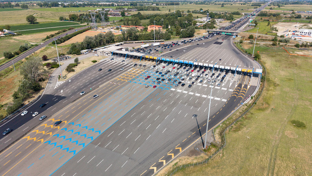 Aerial view of the Autostrada A1 Melegnano toll plaza featuring multiple vehicle lanes traffic flow and highway infrastructure in Melegnano Lombardy Italy.