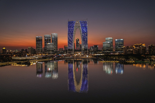 Aerial view of the illuminated Gate to the East skyscraper and modern skyline reflected in Jinji Lake at dusk Suzhou Jiangsu China.