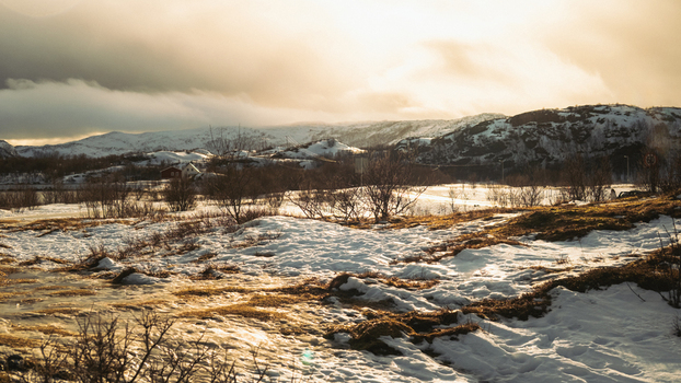 View of a golden landscape with snow meeting the barren earth under a sky heavy with clouds painting a serene cold scene Brensholmen Troms Norway. View of a golden landscape with snow meeting the barren earth under a sky heavy with clouds painting a serene cold scene Brensholmen Troms Norway.