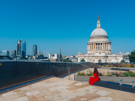 View of a solitary figure in a vibrant red dress overlooking the majestic St Paul s Cathedral and the gleaming London skyline under a clear blue sky London England United Kingdom. View of a solitary figure in a vibrant red dress overlooking the majestic St Paul s Cathedral and the gleaming London skyline under a clear blue sky London England United Kingdom.