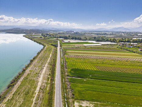 Aerial view of a road running alongside Liqeni Thanes lake and vibrant agricultural fields with greenhouses under a clear blue sky Lushnje Fier County Albania. Aerial view of a road running alongside Liqeni Thanes lake and vibrant agricultural fields with greenhouses under a clear blue sky Lushnje Fier County Albania.