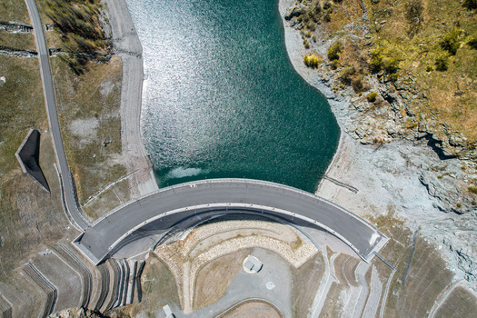 Aerial view of the curved Beauregard Dam wall and turquoise reservoir water surrounded by rocky mountain slopes Valgrisenche Aosta Valley Italy.