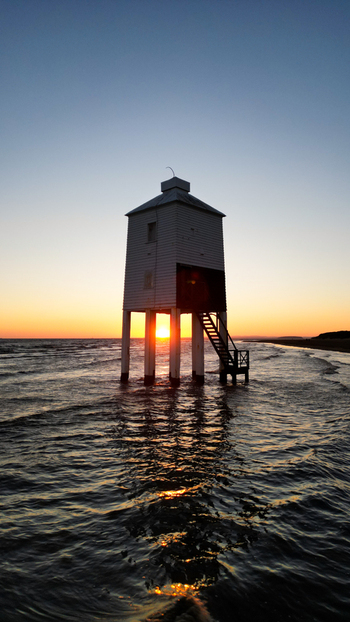 Aerial view of the Burnham on Sea Low Lighthouse standing in the sea at sunset with the sun glowing between its legs calm water and clear sky in Burnham on Sea England United Kingdom. Aerial view of the Burnham on Sea Low Lighthouse standing in the sea at sunset with the sun glowing between its legs calm water and clear sky in Burnham on Sea England United Kingdom.