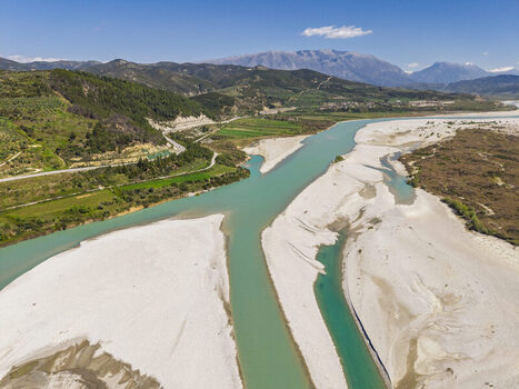 Aerial view of Vjosa Wild River National Park featuring turquoise river channels winding through gravel banks surrounded by green hills in Permet Gjirokaster County Albania. Aerial view of Vjosa Wild River National Park featuring turquoise river channels winding through gravel banks surrounded by green hills in Permet Gjirokaster County Albania.