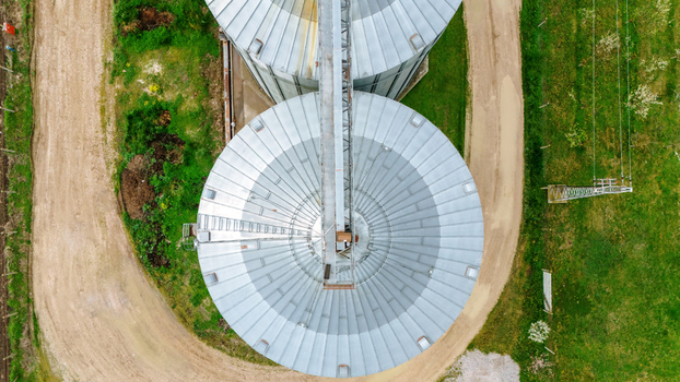 Aerial view of the metallic grain silos stand in contrast to the surrounding green fields and dirt paths Sremska Mitrovica Vojvodina Serbia. Aerial view of the metallic grain silos stand in contrast to the surrounding green fields and dirt paths Sremska Mitrovica Vojvodina Serbia.
