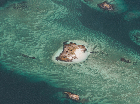 Aerial view of a small island with a white sandy beach surrounded by turquoise water and rocky seabed patterns in Senja Troms Norway.