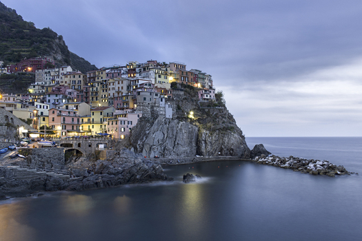 View of the colorful houses of Manarola perched on a rocky cliff overlooking the sea at twilight in Manarola Liguria Italy. View of the colorful houses of Manarola perched on a rocky cliff overlooking the sea at twilight in Manarola Liguria Italy.