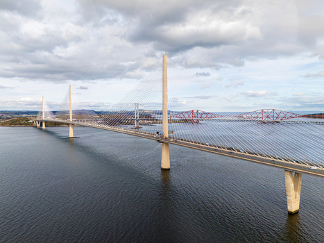 Aerial view of the Queensferry Crossing Bridge spanning the Firth of Forth with the historic Forth Bridge in the background under a cloudy sky in South Queensferry United Kingdom.