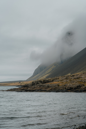 View of the dramatic Stokksnes headland shrouded in low hanging clouds above the rocky coastline and dark sea in Iceland.