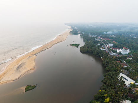 Aerial view of the coastline with a sandy beach separating the ocean from a calm lagoon surrounded by lush palm trees and coastal buildings in Galle Southern Province Sri Lanka.