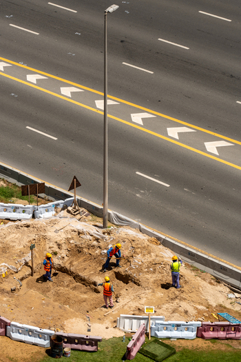 Aerial view of construction workers in safety vests digging a trench next to a multi lane highway with yellow road markings and a lamp post in Dubai Dubai United Arab Emirates. Aerial view of construction workers in safety vests digging a trench next to a multi lane highway with yellow road markings and a lamp post in Dubai Dubai United Arab Emirates.
