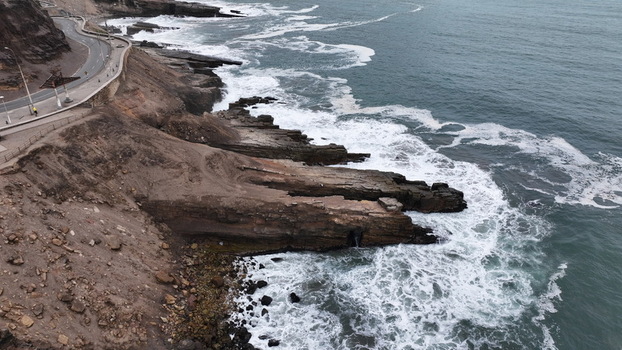 Aerial view of the rugged coastline with dramatic cliffs crashing ocean waves and a winding coastal road in Chorrillos Provincia de Lima Peru.