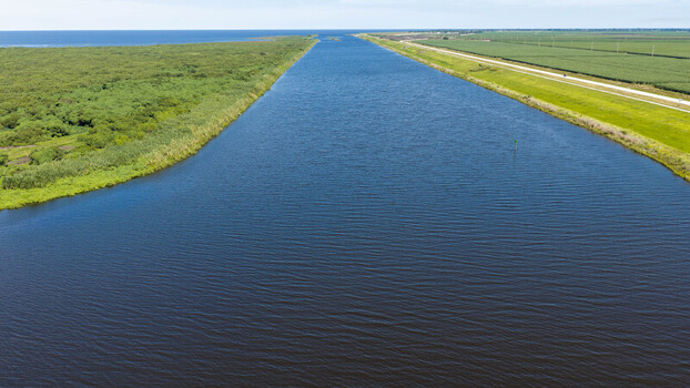 Aerial view of the canal near Pahokee with lush green vegetation on one side and agricultural fields on the other under a clear blue sky Pahokee Florida United States. Aerial view of the canal near Pahokee with lush green vegetation on one side and agricultural fields on the other under a clear blue sky Pahokee Florida United States.