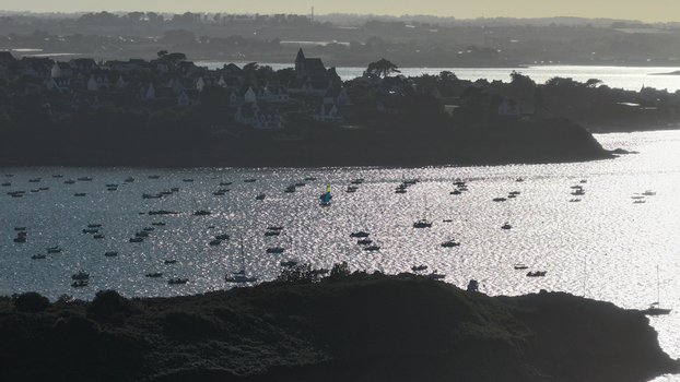 Aerial view of boats dotting the shimmering waters near the town a silhouette foreground framing the sun kissed bay Carantec Finistre France.