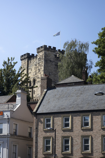 View of the historic Newcastle Castle keep with a flag flying against a clear blue sky rising above traditional brick buildings in Newcastle upon Tyne England United Kingdom. View of the historic Newcastle Castle keep with a flag flying against a clear blue sky rising above traditional brick buildings in Newcastle upon Tyne England United Kingdom.