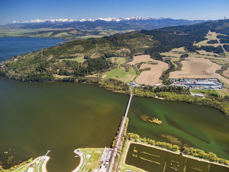 Aerial view of Oravska priehrada reservoir featuring a long bridge green hills and snow capped mountains in the distance Namestovo Zilinsky kraj Slovakia. Aerial view of Oravska priehrada reservoir featuring a long bridge green hills and snow capped mountains in the distance Namestovo Zilinsky kraj Slovakia.