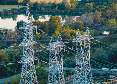 Aerial view of high voltage transmission pylons and power lines surrounded by lush vegetation near an industrial energy complex in Trino Piedmont Italy. Aerial view of high voltage transmission pylons and power lines surrounded by lush vegetation near an industrial energy complex in Trino Piedmont Italy.