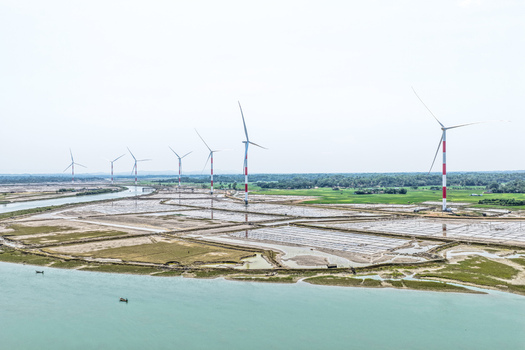Aerial view of wind turbines standing tall against the horizon juxtaposed with textured land and the serene blue waters Cox s Bazar Chittagong Division Bangladesh. Aerial view of wind turbines standing tall against the horizon juxtaposed with textured land and the serene blue waters Cox s Bazar Chittagong Division Bangladesh.