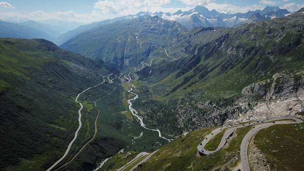 Aerial view of Furka Pass winding through a deep alpine valley with steep green slopes and snow capped peaks in Obergoms Valais Switzerland. Aerial view of Furka Pass winding through a deep alpine valley with steep green slopes and snow capped peaks in Obergoms Valais Switzerland.