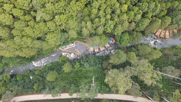 Aerial view of Hutan Pinus Rahong featuring a winding river small wooden structures nestled among dense pine trees and a dirt road in Pangalengan West Java Indonesia. Aerial view of Hutan Pinus Rahong featuring a winding river small wooden structures nestled among dense pine trees and a dirt road in Pangalengan West Java Indonesia.