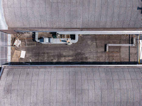 Aerial view of a flat industrial roof section between two corrugated metal roofs with ventilation equipment and pipes in Casale Monferrato Piedmont Italy. Aerial view of a flat industrial roof section between two corrugated metal roofs with ventilation equipment and pipes in Casale Monferrato Piedmont Italy.