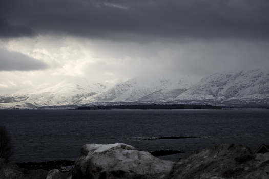 View of snow capped mountains and dark storm clouds over the cold waters of a fjord in Kvaloya Troms Norway. View of snow capped mountains and dark storm clouds over the cold waters of a fjord in Kvaloya Troms Norway.