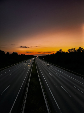 Aerial view of a highway at sunset with cars driving along the road under a vibrant orange and purple sky in Sehnde Germany.