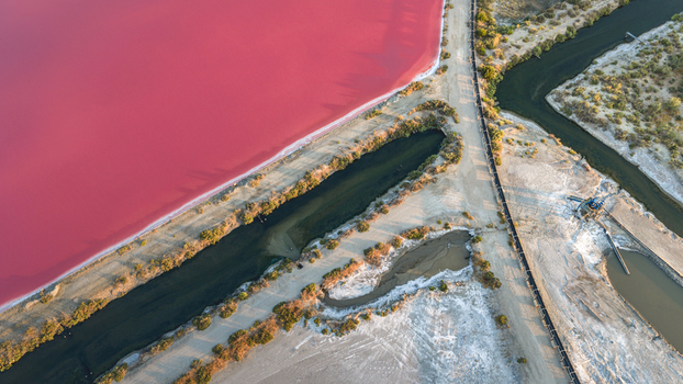 Aerial view of a vibrant pink salt evaporation pond bordered by dark water channels mineral deposits and dry embankments in Aigues Mortes Occitanie France.