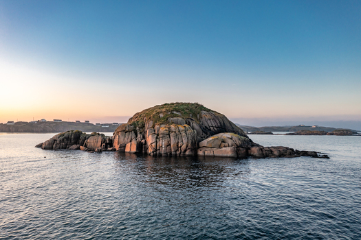 Aerial view of a rocky island surrounded by calm sea waters at sunset with distant coastal houses in Kincasslagh County Donegal Ireland. Aerial view of a rocky island surrounded by calm sea waters at sunset with distant coastal houses in Kincasslagh County Donegal Ireland.
