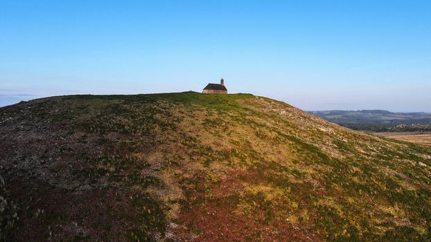 Aerial view of Chapelle Saint Michel de Brasparts sitting atop a grassy hill under a clear blue sky in Saint Rivoal Bretagne France. Aerial view of Chapelle Saint Michel de Brasparts sitting atop a grassy hill under a clear blue sky in Saint Rivoal Bretagne France.