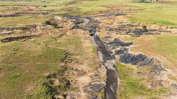 Aerial view of a winding riverbed with dark soil and eroded banks cutting through the green hills and rural landscape of Pietermaritzburg KwaZulu Natal South Africa.