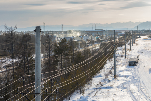 Aerial view of power lines stretching across a snowy landscape with sparse trees and a distant town in Severobaykalsk Buryatia Russia.