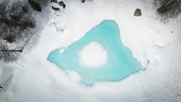 Aerial view of a striking turquoise lake sits nestled amidst a blanket of fresh snow in Arpy Valle d Aosta Italy. Aerial view of a striking turquoise lake sits nestled amidst a blanket of fresh snow in Arpy Valle d Aosta Italy.