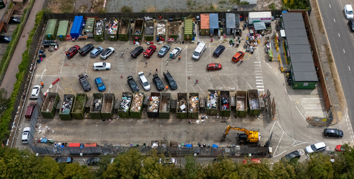 Aerial view of Stevenage Recycling Centre with rows of waste skips parked cars and an excavator in a busy waste management facility in Stevenage England United Kingdom.