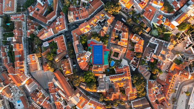 Aerial view of a vibrant blue sports court nestled among historic terracotta tiled rooftops and narrow streets in a dense urban neighborhood in Portugal.