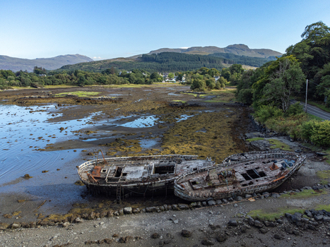 Aerial view of weathered boats rest on the Isle of Mull s shore a stark contrast against the lush hills and clear sky Salens ships United Kingdom. Aerial view of weathered boats rest on the Isle of Mull s shore a stark contrast against the lush hills and clear sky Salens ships United Kingdom.