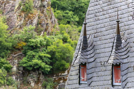 View of the slate roof and spires of Eltz Castle featuring red shutters and lush green forest in Wierschem Rhineland Palatinate Germany.