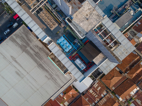 Aerial view of a building rooftop featuring industrial HVAC units cooling towers and ventilation systems surrounded by urban residential rooftops in Purwokerto Central Java Indonesia. Aerial view of a building rooftop featuring industrial HVAC units cooling towers and ventilation systems surrounded by urban residential rooftops in Purwokerto Central Java Indonesia.