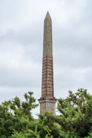 View of the Bodmin Beacon obelisk monument rising above green bushes under a cloudy sky in Bodmin Cornwall United Kingdom. View of the Bodmin Beacon obelisk monument rising above green bushes under a cloudy sky in Bodmin Cornwall United Kingdom.