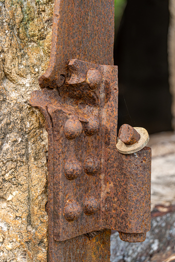 View of a weathered rusted metal hinge attached to a stone structure at the historic North Field Base in Northern Tinian Tinian Northern Mariana Islands. View of a weathered rusted metal hinge attached to a stone structure at the historic North Field Base in Northern Tinian Tinian Northern Mariana Islands.