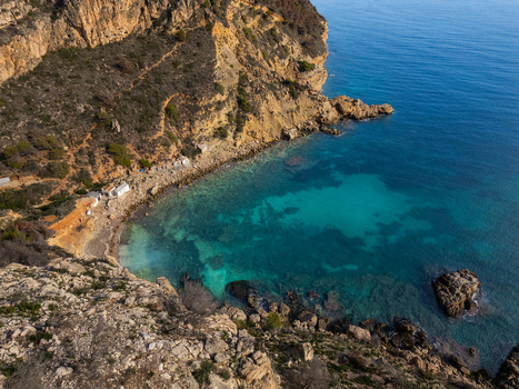 Aerial view of Cala Llebeig with its turquoise waters rocky cliffs and small white fishermen huts along the shore in El Poble Nou de Benitatxell Valencian Community Spain.