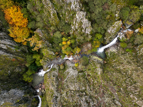 Aerial view of Poco do Inferno waterfall cascading through a rocky gorge surrounded by autumn foliage and lush forest in Manteigas Guarda District Portugal. Aerial view of Poco do Inferno waterfall cascading through a rocky gorge surrounded by autumn foliage and lush forest in Manteigas Guarda District Portugal.