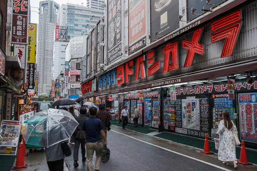 Tokyo Japan 01 October 2025 View of a bustling street with Yodobashi Camera s vibrant red sign contrasting against the overcast sky as pedestrians with umbrellas navigate the wet pavement. Tokyo Japan 01 October 2025 View of a bustling street with Yodobashi Camera s vibrant red sign contrasting against the overcast sky as pedestrians with umbrellas navigate the wet pavement.