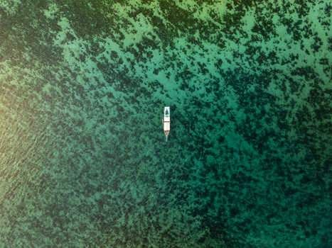 Aerial view of a small traditional boat floating on crystal clear turquoise water above vibrant coral reefs in Komodo National Park Komodo East Nusa Tenggara Indonesia. Aerial view of a small traditional boat floating on crystal clear turquoise water above vibrant coral reefs in Komodo National Park Komodo East Nusa Tenggara Indonesia.